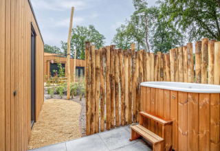 Udendørs wellnessområde med træbadekar, rustik afskærmning og moderne træhytter på Holiday Park De IJsvogel.