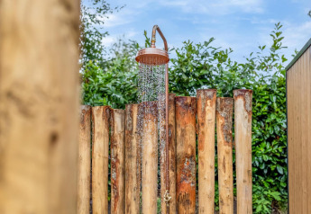 Udendørs bruser ved Tiny Wellness Suite i Holiday Park De IJsvogel, omgivet af træ og grøn beplantning.