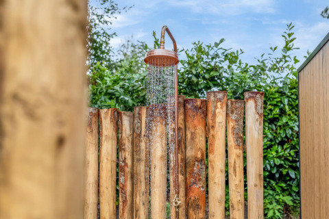 Udendørs bruser ved Tiny Wellness Suite i Holiday Park De IJsvogel, omgivet af træ og grøn beplantning.