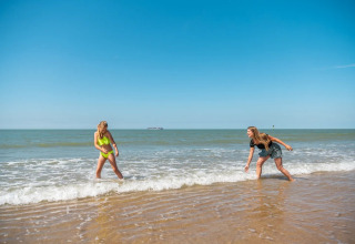 To kvinder leger i vandkanten på stranden under blå himmel ved EuroParcs De Zeeuwse Duinen i Zeeland.