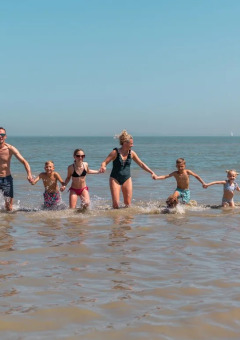 Familie genießt einen Tag am Strand im Wasser bei EuroParcs De Zeeuwse Duinen, Ferienpark in Zeeland, Niederlande.