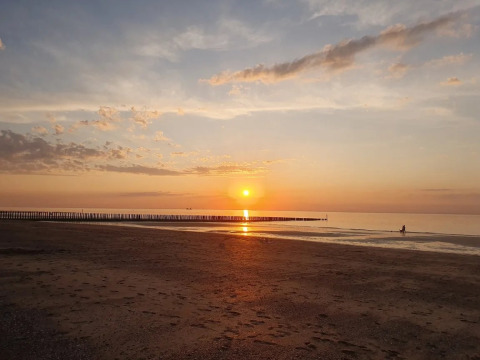 Puesta de sol en la playa en EuroParcs De Zeeuwse Duinen en Zeeland, Países Bajos, con mar tranquilo.