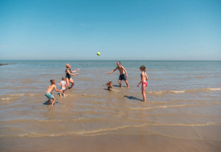 En familie leger med en bold i vandet på stranden ved EuroParcs De Zeeuwse Duinen i Zeeland, Holland.