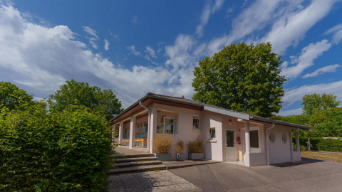 Vakantieparkgebouw Camping Seasonova Vittel, omgeven door bomen en blauwe lucht in Grand Est, Frankrijk.