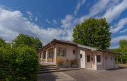Vakantieparkgebouw Camping Seasonova Vittel, omgeven door bomen en blauwe lucht in Grand Est, Frankrijk.