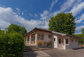 Vakantieparkgebouw Camping Seasonova Vittel, omgeven door bomen en blauwe lucht in Grand Est, Frankrijk.