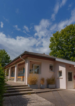 Edificio del parque vacacional Camping Seasonova Vittel, rodeado de árboles y cielo azul en Grand Est, Francia.
