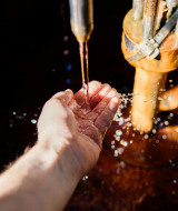 Una mano recoge agua de un grifo exterior cerca de Vittel, Grand Est, Francia, bajo la luz del sol.