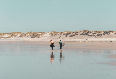 Dos personas caminan por la playa cerca de Trelevern, Bretaña, Francia, con dunas y cielo claro de fondo.