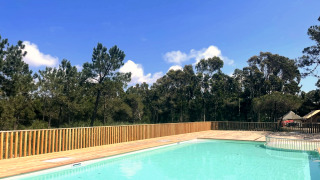 Udendørs swimmingpool med træterrasse og udsigt til skov, solrig dag i Village Huttopia Lagoa de Óbidos.