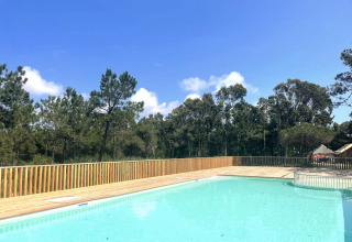 Udendørs swimmingpool med træterrasse og udsigt til skov, solrig dag i Village Huttopia Lagoa de Óbidos.