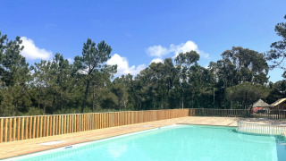 Piscina al aire libre con terraza de madera y vistas al bosque en un día soleado en Village Huttopia Lagoa de Óbidos.