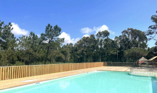 Piscina al aire libre con terraza de madera y vistas al bosque en un día soleado en Village Huttopia Lagoa de Óbidos.