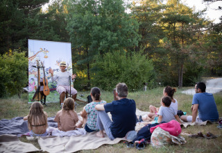 Familier og børn sidder på tæpper i naturen og lytter til en historiefortæller ved Village Huttopia Lagoa de Óbidos.