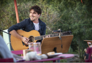 Ein Mann spielt Gitarre und singt draußen im Ferienpark Village Huttopia Lagoa de Óbidos in Zentralportugal.