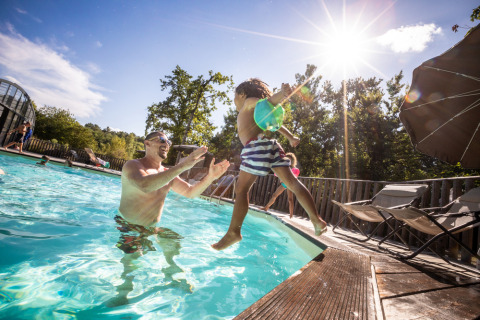 Un hombre juega con un niño que salta a la piscina en un día soleado en Village Huttopia Lagoa de Óbidos.