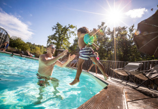 A man plays with a child jumping into the pool on a sunny day at Village Huttopia Lagoa de Óbidos, Portugal.