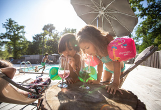 Deux enfants avec des brassards boivent des boissons colorées près de la piscine à Huttopia Lagoa de Óbidos, Portugal.