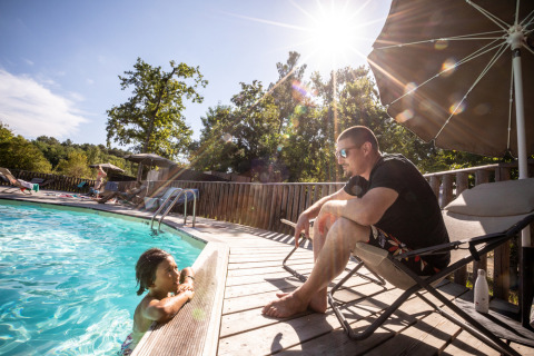 Hombre relajado en una silla junto a la piscina, mientras un niño nada. Día soleado en un parque de Portugal.