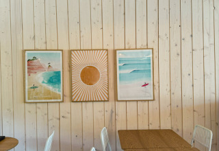 Lyst, moderne caféområde hos Village Huttopia Lagoa de Óbidos med træpaneler, kunst og hvide stole.