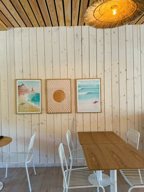 Lichte, moderne caféhoek in Village Huttopia Lagoa de Óbidos met houten panelen, kunst en witte stoelen.