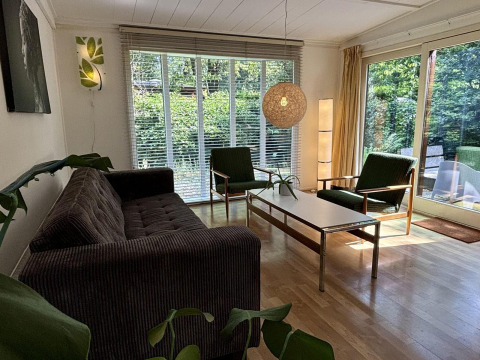 Wohnzimmer im Retro Lodge im Bungalowpark Het Verscholen Dorp, Niederlande, mit großen Fenstern und Retro-Möbeln.