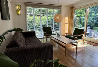 Woonkamer in Retro Lodge bij Bungalowpark Het Verscholen Dorp, Nederland, met grote ramen en retro meubilair.