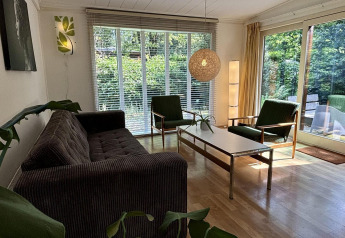 Woonkamer in Retro Lodge bij Bungalowpark Het Verscholen Dorp, Nederland, met grote ramen en retro meubels.