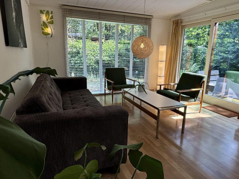 Wohnzimmer der Retro Lodge im Bungalowpark Het Verscholen Dorp mit großen Fenstern, Retro-Möbeln und Ausblick.