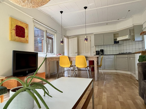 Acogedora cabaña con cocina moderna, sillas amarillas y planta en Retro Lodge, Het Verscholen Dorp, Países Bajos.