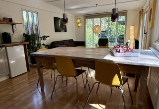 Woonruimte met houten tafel, gele stoelen en grote ramen in Retro Lodge, Bungalowpark Het Verscholen Dorp, Nederland.