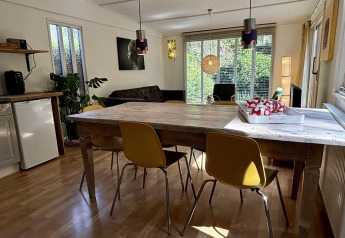 Woonruimte met houten tafel, gele stoelen en grote ramen in Retro Lodge, Bungalowpark Het Verscholen Dorp, Nederland.
