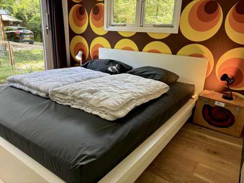 Schlafzimmer im Retro Lodge, Bungalowpark Het Verscholen Dorp, Niederlande, mit Retro-Tapete und Bett.