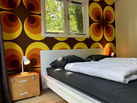 Retro Lodge slaapkamer met opvallend jaren 70-behang en zwart bed bij Bungalowpark Het Verscholen Dorp.