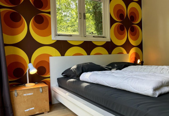 Retro Lodge slaapkamer met opvallend jaren 70-behang en zwart bed bij Bungalowpark Het Verscholen Dorp.