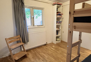 Værelse i Retro Lodge på Bungalowpark Het Verscholen Dorp, Holland, med køjeseng, stol og reol.
