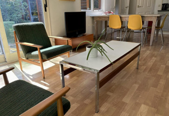 Woonkamer in Retro Lodge bij Bungalowpark Het Verscholen Dorp met groene fauteuils en gele stoelen.