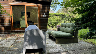 Patio exterior en Retro Lodge con sofá verde, silla moderna y vistas a cabaña de madera y jardín frondoso.