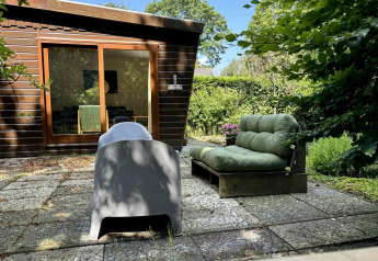 Buitenterras bij Retro Lodge met groene loungebank, moderne stoel en uitzicht op houten huis en tuin.