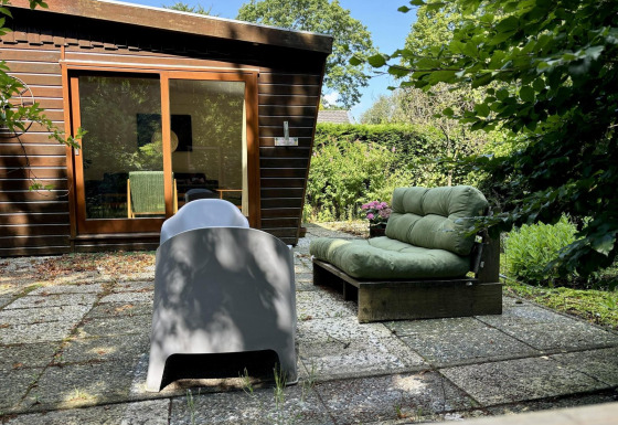 Buitenterras bij Retro Lodge met groene loungebank, moderne stoel en uitzicht op houten huis en tuin.