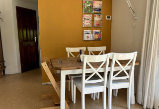 Eethoek met houten tafel, witte stoelen en gele muur in Tiny Lodge Basic bij Het Verscholen Dorp, Nederland.