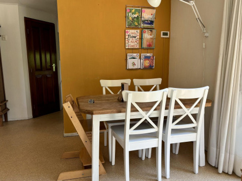 Comedor con mesa de madera, sillas blancas y pared amarilla en Tiny Lodge Basic en Het Verscholen Dorp, Países Bajos.