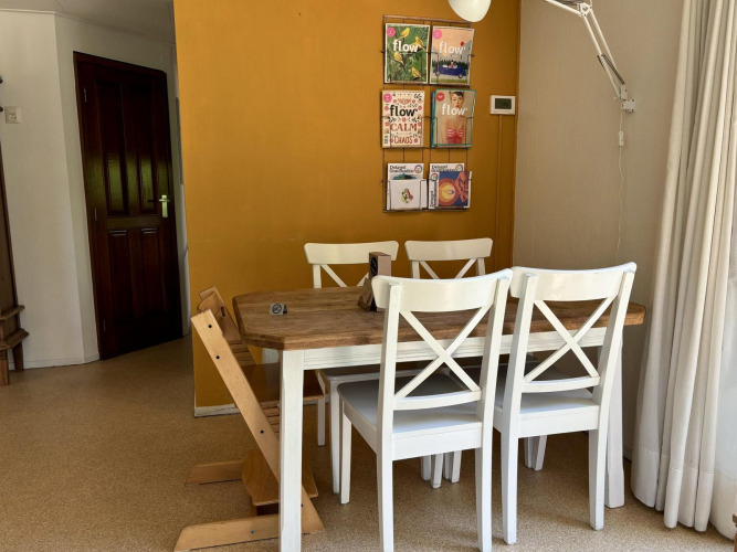 Comedor con mesa de madera, sillas blancas y pared amarilla en Tiny Lodge Basic en Het Verscholen Dorp, Países Bajos.