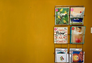 Revistero en pared mostaza con revistas Flow y Delayed Gratification en Tiny Lodge Basic, Países Bajos.