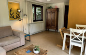 Sala en Tiny Lodge Basic de Bungalowpark Het Verscholen Dorp con sofá, mesa de comedor y armario antiguo.