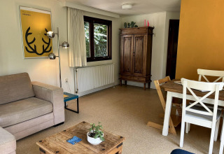 Sala en Tiny Lodge Basic de Bungalowpark Het Verscholen Dorp con sofá, mesa de comedor y armario antiguo.