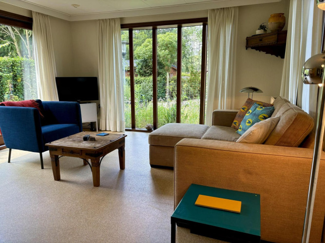 Sala de estar en Tiny Lodge Basic, Bungalowpark Het Verscholen Dorp, con sofá, sillón y vista al jardín.