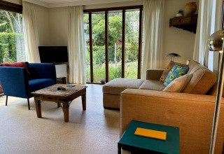 Sala de estar en Tiny Lodge Basic, Bungalowpark Het Verscholen Dorp, con sofá, sillón y vista al jardín.