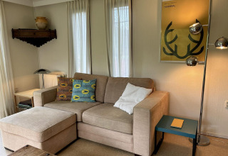 Sala acogedora con sofá beige, cojines coloridos, póster amarillo y lámpara en Tiny Lodge Basic, Países Bajos.