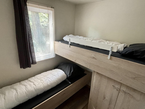 Habitación con literas y ventana con cortina oscura en Tiny Lodge Basic del Bungalowpark Het Verscholen Dorp, Países Bajos.